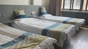 A hotel room with two single beds, a nightstand, a window with curtains, and a view of buildings outside.