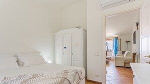A bedroom with a bed, a wardrobe, and a chair in a well-lit room with tiled flooring. - Casa Lulù with seaview and shared pool (Tertenia)