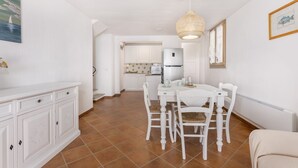 A spacious kitchen with white cabinets, a dining table with chairs, and a hanging light fixture. - Casa Lulù with seaview and shared pool (Tertenia)