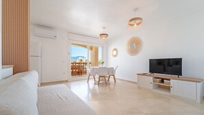 Une pièce spacieuse comprenant un lit, un téléviseur posé sur un meuble en bois, une table à manger avec des chaises, et une vue à travers une porte vitrée.