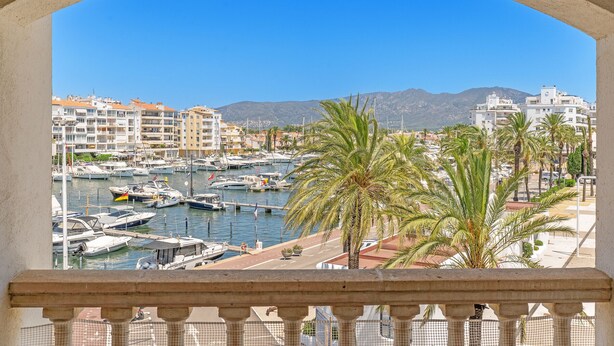 Un port de plaisance avec des bateaux, un ciel bleu clair et des bâtiments en arrière-plan.