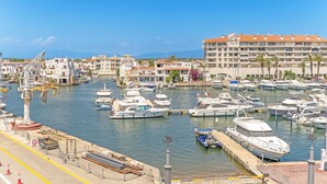 Un port de plaisance où sont amarrés de nombreux bateaux, un grand immeuble doté de balcons et un ciel dégagé.