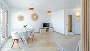 Un espace repas moderne avec une table ronde, des chaises blanches, un téléviseur et des lampes fixées au mur.
