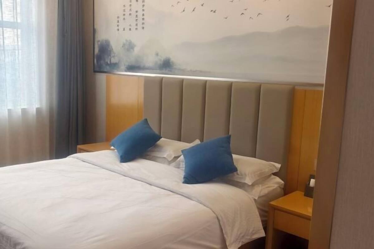 Een hotelkamer met een bed, twee kussens, een nachtkastje en een muurschildering.