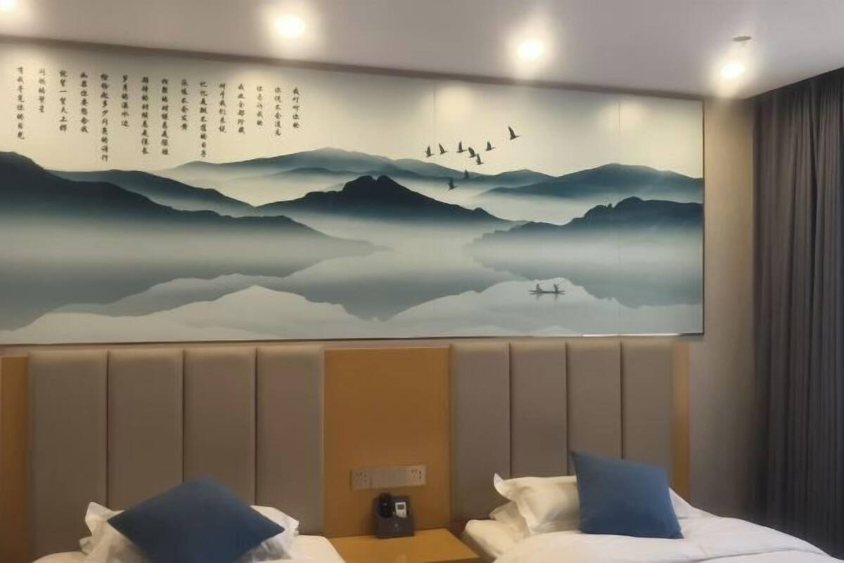 Hotelkamer met een groot muurschildering van bergen en vogels, een bed met witte beddengoed en blauwe kussens, en een nachtkastje met een telefoon.