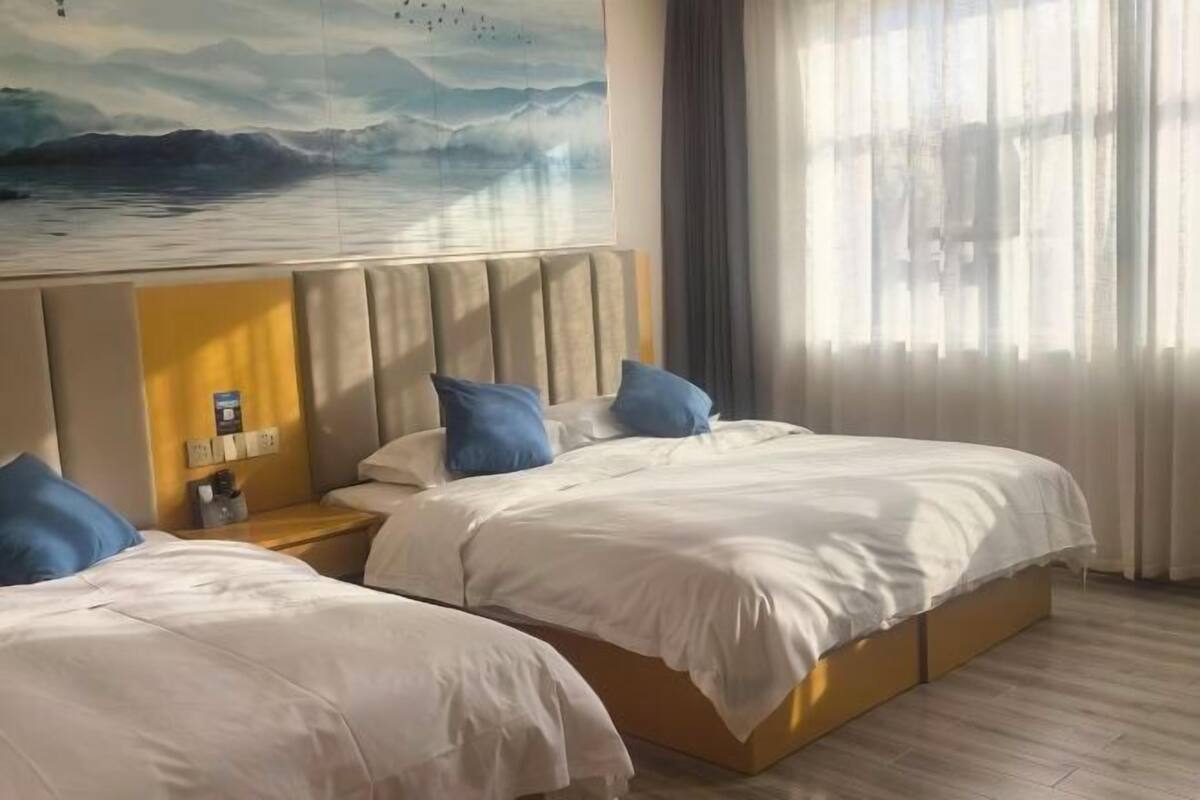 Een hotelkamer met twee bedden, een schilderij van een zeegezicht, een nachtkastje met een lamp en een raam met gordijnen.