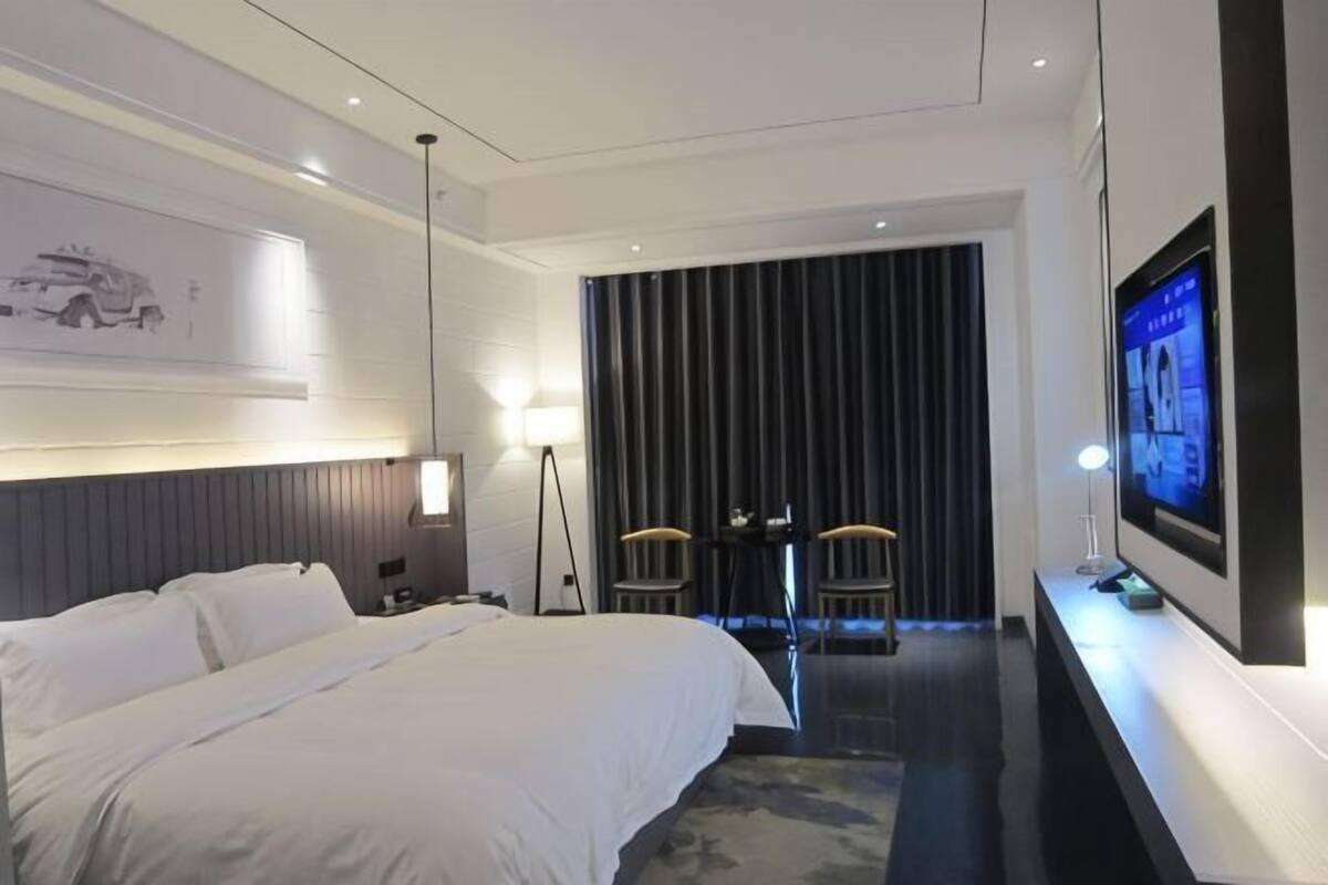 Een hotelkamer met een groot bed, een bureau met twee stoelen, een televisie en een donkere gordijnenachtergrond.