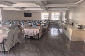 A conference room with rows of tables and chairs, a long counter with kitchen appliances, and a large screen on the wall. - Yuanfang Hotel (Zhenglan Banner)