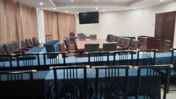 Una sala de conferencias con una mesa larga y sillas, un televisor de pantalla plana y una puerta de madera.