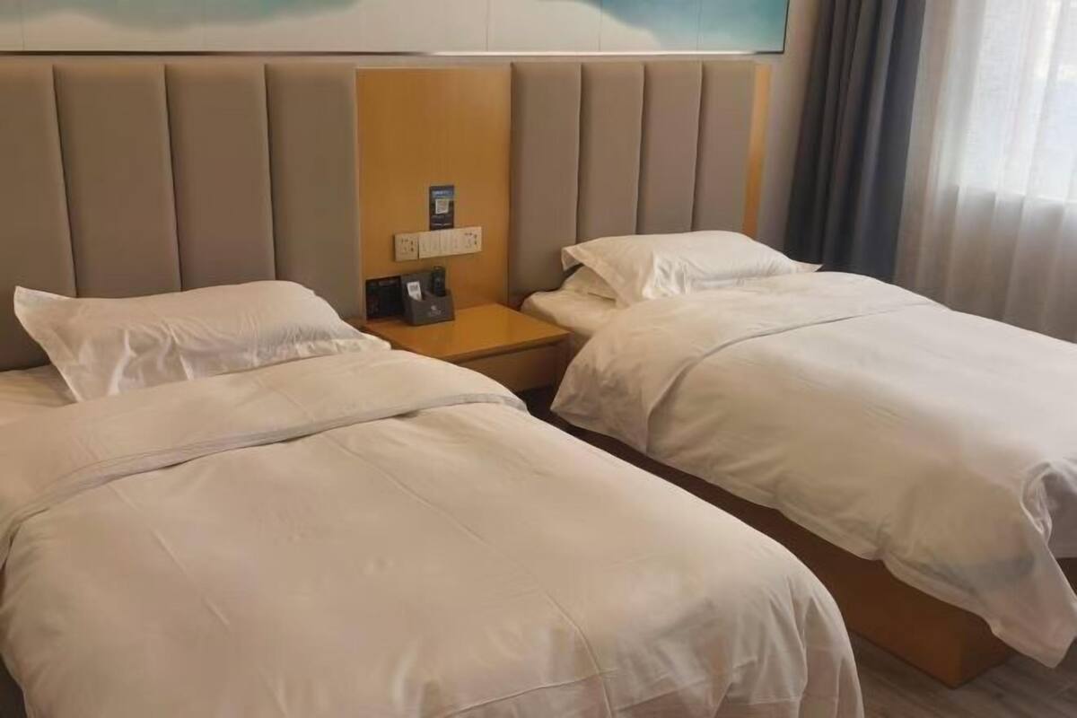 Een hotelkamer met twee bedden, een hoofdeinde, een nachtkastje met een lamp en een schilderij aan de muur.