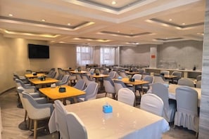 A conference room with multiple tables and chairs, a flat-screen TV on the wall, and a large window.