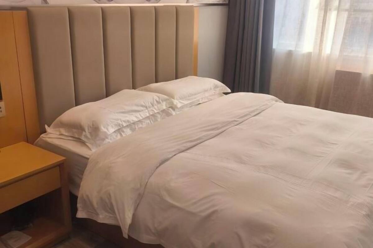 Een hotelkamer met een bed, een nachtkastje van hout en een hoofdbord.