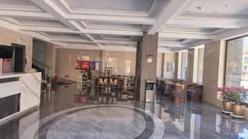 Un vestíbulo de hotel con piso de mármol, una recepción, área de descanso y ventanas amplias.