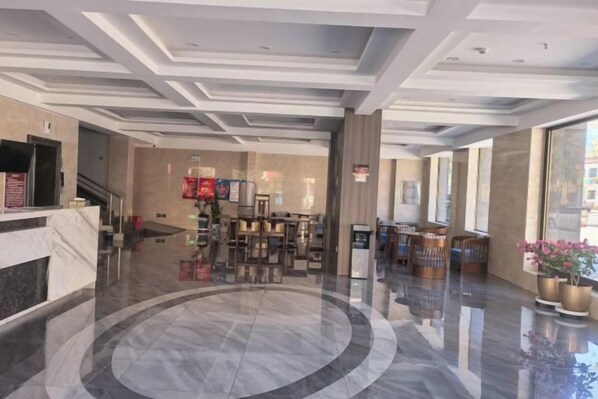 Un vestíbulo de hotel con piso de mármol, una recepción, área de descanso y ventanas amplias.