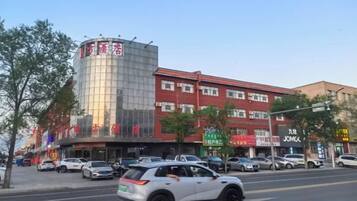 A multi-story building with commercial establishments on the ground floor, a parking lot in front, and a clear sky.