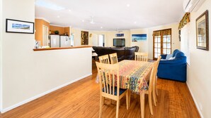 A modern living room with a dining table, a sofa, and a kitchen area with a refrigerator and a television. - Hidden Gem Getaway in Dunsboroughs Heart (Dunsborough)