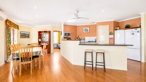 A modern kitchen with a central island, wooden dining table, and chairs, connected to a living area with a ceiling fan. - Hidden Gem Getaway in Dunsboroughs Heart (Dunsborough)