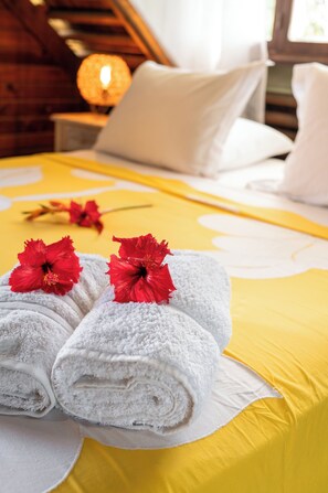A neatly made bed with white towels and red flowers, a yellow bedspread, and a lamp in the background. - GREAT HOUSE BY MANAEVA LODGE (Moorea-Maiao)