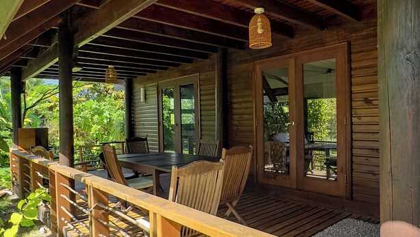 An outdoor wooden deck with a table and chairs, surrounded by greenery. - GREAT HOUSE BY MANAEVA LODGE (Moorea-Maiao)