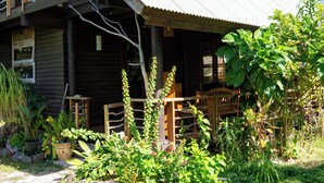 A rustic wooden cabin with a porch, surrounded by lush greenery and potted plants. - GREAT HOUSE BY MANAEVA LODGE (Moorea-Maiao)