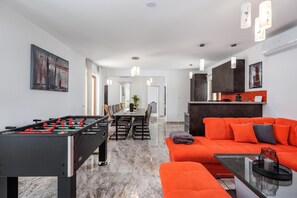 Un espace de vie moderne avec un baby-foot, un canapé orange vif et une table basse en verre.