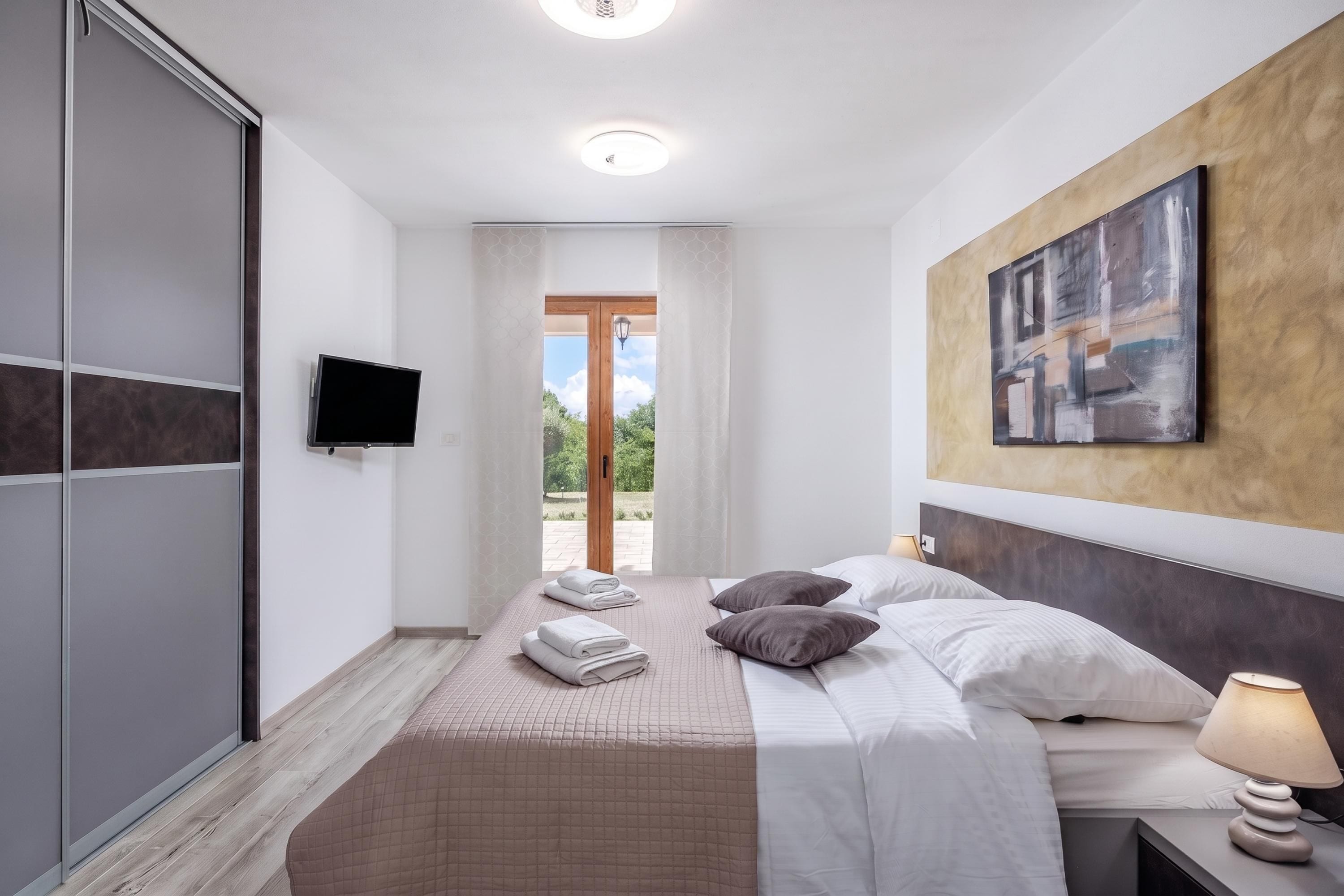 Quarto de hotel com cama, televisão, quadro e vista para o exterior.