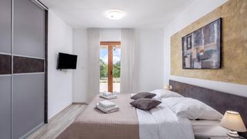 Quarto de hotel com cama, televisão, quadro e vista para o exterior.