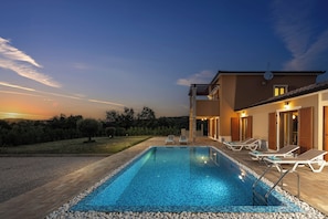 A swimming pool with lounge chairs, a building with a tiled roof, and a sunset in the background. - Villa Erla (Sveta Nedelja)
