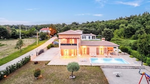Una casa de dos pisos con piscina, un porche cubierto y un jardín bien cuidado.