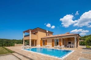 Una casa de dos pisos con piscina, mobiliario de exterior y un patio.