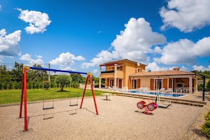 Una casa con piscina, un conjunto de columpios y un patio.