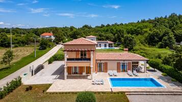 Uma casa de dois andares com piscina, cercada por vegetação.