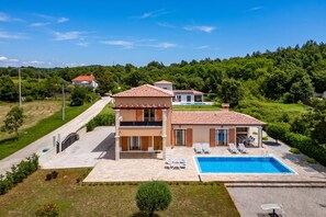 Une maison à deux étages avec une piscine, entourée de verdure.
