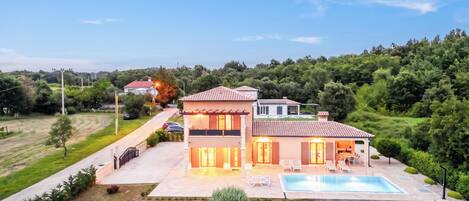 A two-story house with a swimming pool, a covered patio, and a well-maintained garden.