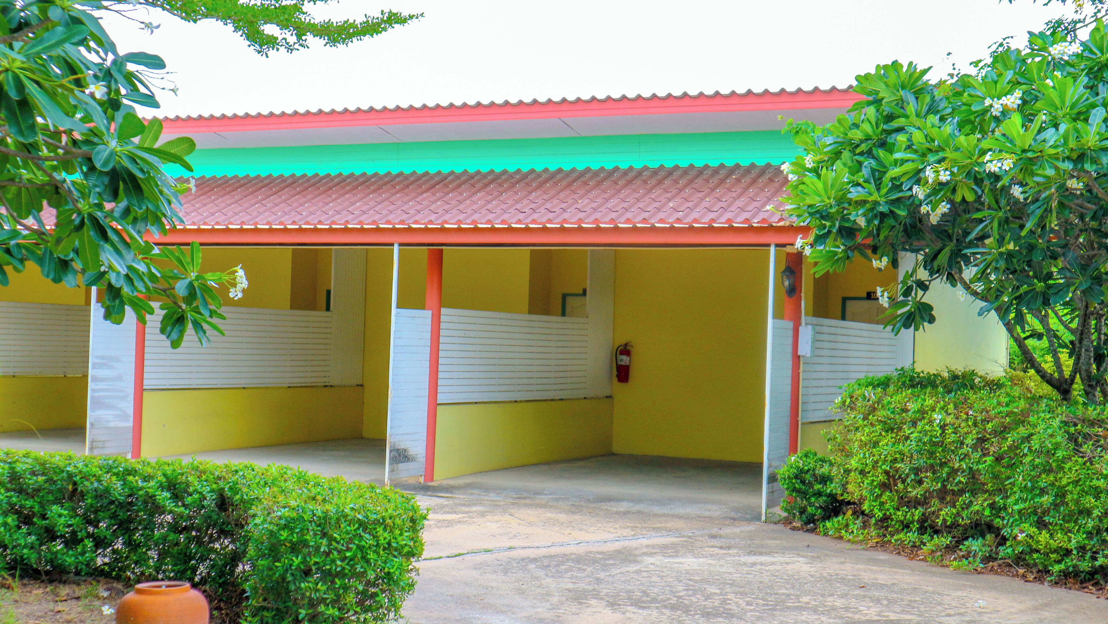 A building with a red roof and yellow walls, featuring a covered entrance area with a concrete floor.