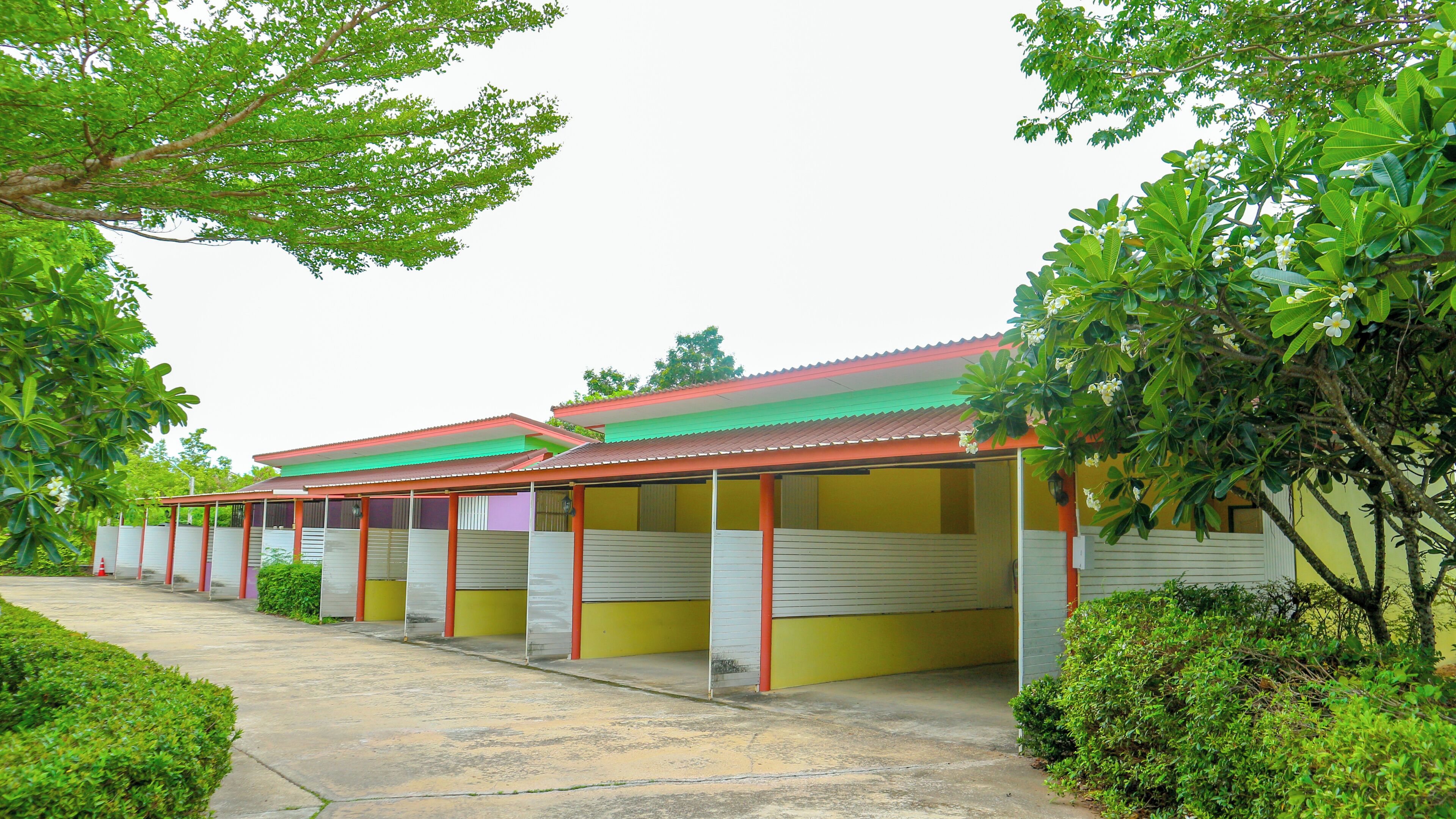 A row of single-story buildings with a red roof, yellow walls, and a covered walkway.