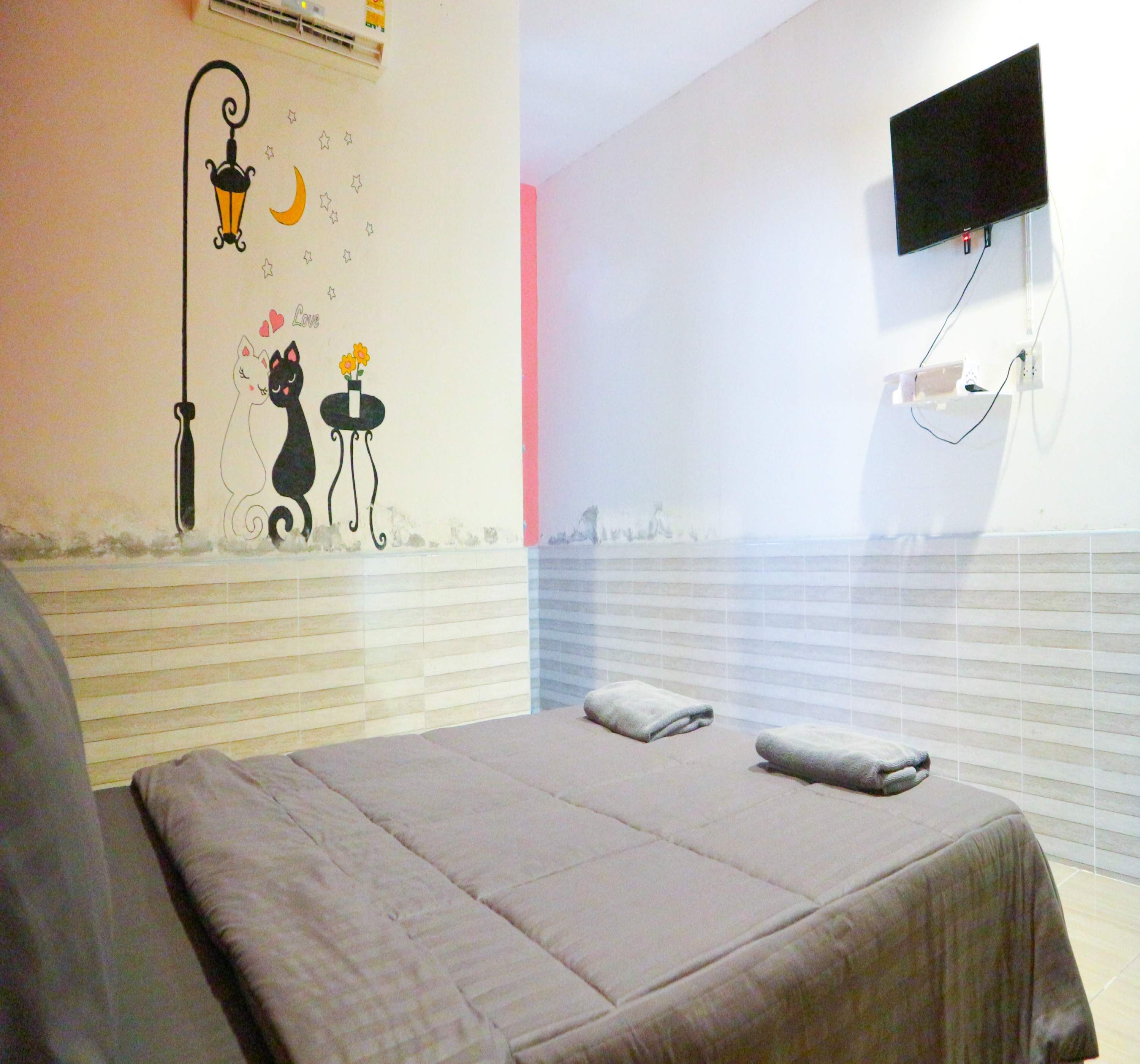 A bedroom with a bed, a wall-mounted TV, and a decorative wall with a cat and moon.