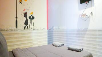A bedroom with a bed, a wall-mounted TV, and a decorative wall with a cat and moon.