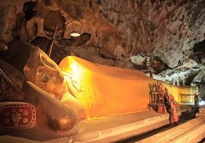 Una gran estatua reclinada de Buda en una cueva, con una plataforma y algunas personas cerca.