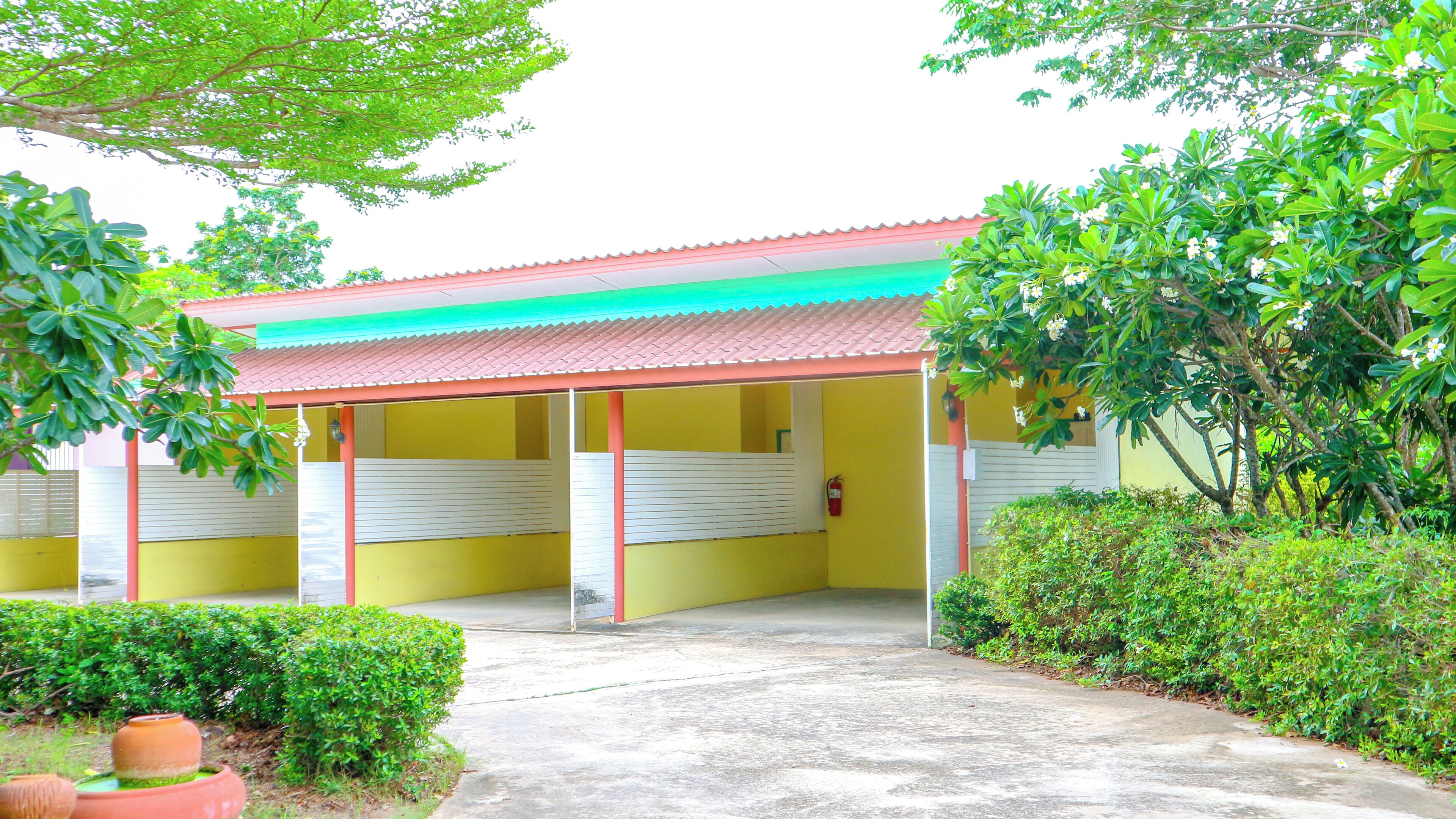 Un edificio con techo rojo y paredes amarillas, rodeado de vegetación.