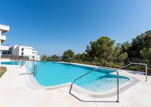 A swimming pool with clear blue water, surrounded by a concrete deck and metal railings.