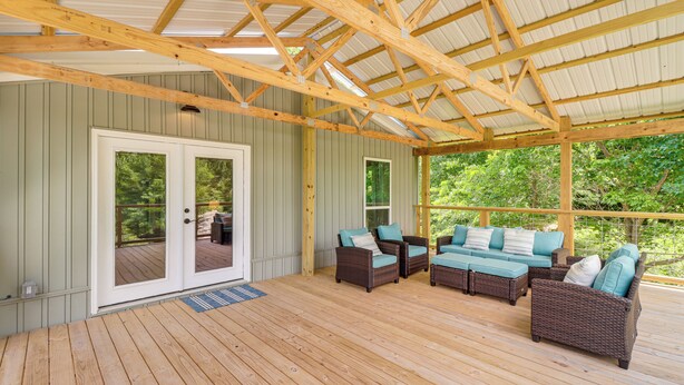 Ein überdachter Außenbereich mit Holzboden, einer Sofagarnitur und einer Glastür zum Deck.