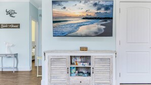 A room with a wooden cabinet, a framed picture of a beach, and a sign that reads "Beach House". - Great Location Near Beach, Walk to Restaurants and shops, Fenced in Back Yard (Oak Island)