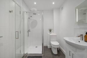Un baño moderno con cabina de ducha de vidrio, inodoro y lavamanos.