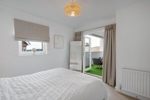 Un dormitorio con cama, ventana con vistas, puerta a un balcón y radiador.