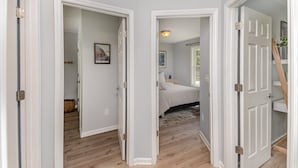 A hallway with white doors leading to a bedroom with a bed and a nightstand. - Relaxing Belmont Escape, 4BR, Pet Friendly (Belmont)