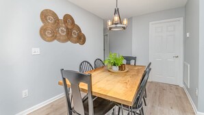 A dining area with a wooden table, black chairs, a hanging light fixture, and a decorative wall piece. - Relaxing Belmont Escape, 4BR, Pet Friendly (Belmont)
