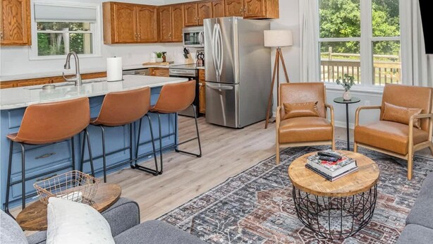 A modern kitchen with wooden cabinets, a stainless steel refrigerator, and a bar area with stools.