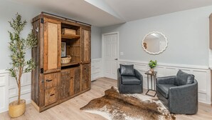 A room with a wooden cabinet, two leather chairs, a cowhide rug, and a potted plant. - Relaxing Belmont Escape, 4BR, Pet Friendly (Belmont)
