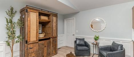 Een kamer met een houten kast, twee lederen stoelen, een koehuidtapijt en een potplant.